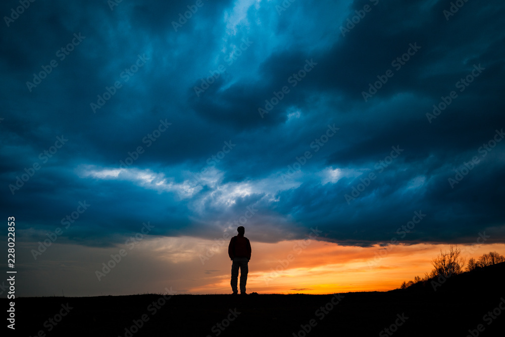 Man silhouette standing against dramatic clouds background