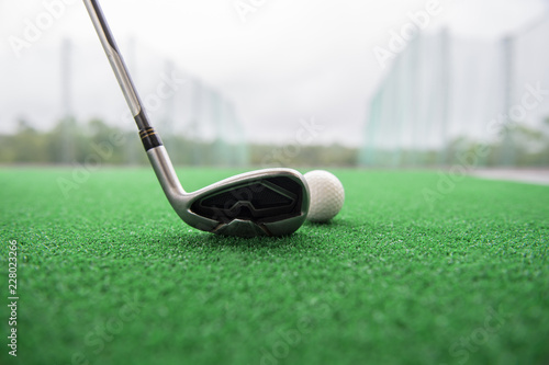 Golf club and ball on a synthetic grass mat at a practice range.