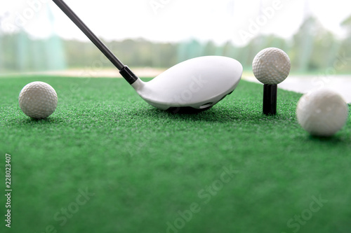 Golf club and balls on a synthetic grass mat at a practice range.