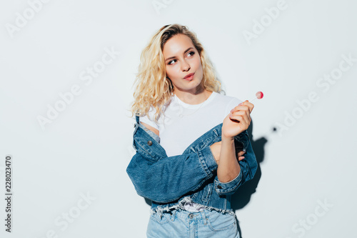 Beauty portrait of a blonde woman eating lollipop and looking away isolated over white background