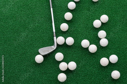Golf club and balls on a synthetic grass mat at a practice range.