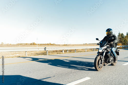 Driver riding motorcycle on empty road out of the city at beautiful autumn time.
