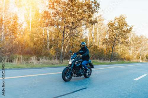 Driver riding motorcycle on empty road in beautiful autumn forest.