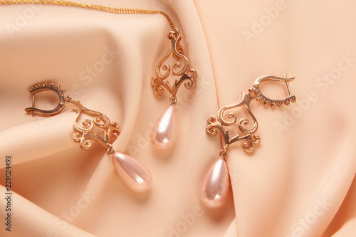 Pearl Golden Necklace and Earrings on beige silk background with copy space. Beautiful precious women's jewelry, close-up, top view