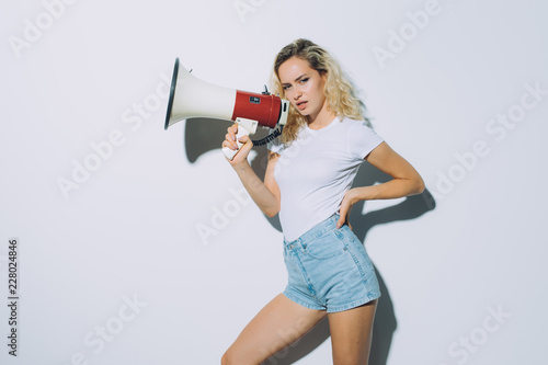 Blonde young woman shouting with a megaphone isolated on a white background