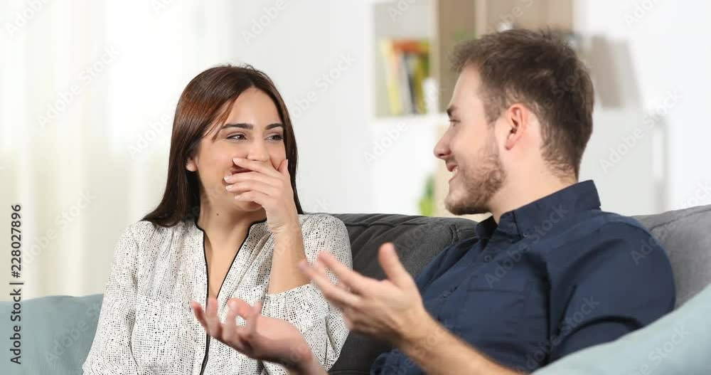 Embarrassed girl talking with a man during a date hiding smile with her hand at home Embarrassed girl talking with a man during a date hiding smile with her hand at home