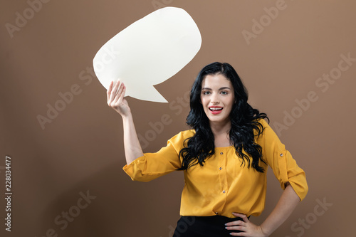 Young woman holding a speech bubble on a solid background © Tierney