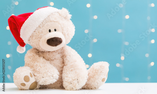 Teddy bear wearing a Santa hat on a shiny light blue background
