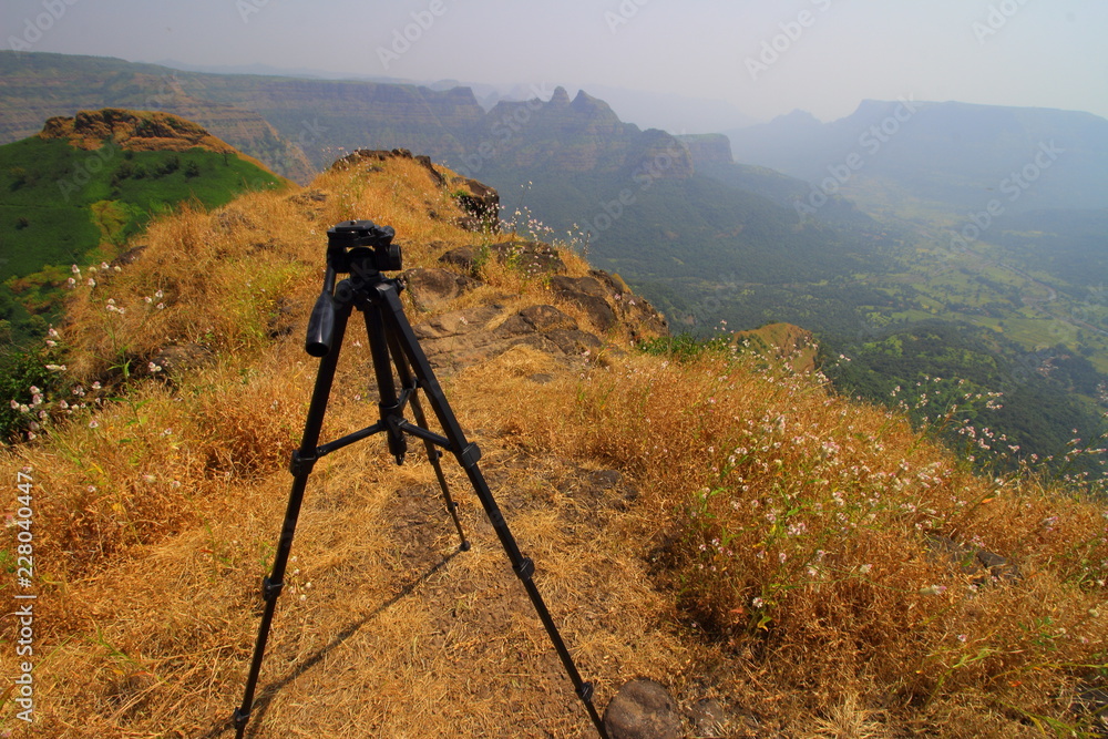 View of a tripod stand with a rugged hilly landscape of the western ghats of Maharashtra, India in the background on a clear day.