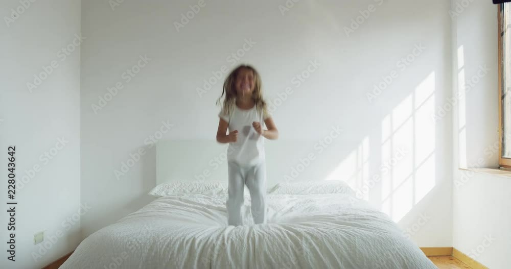 A little girl, wearing white pajamas, jumps on the bed and has fun. A little girl, wearing white pajamas, jumps on the bed and has fun.