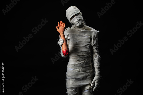Fototapeta Studio shot portrait  of young man in costume  dressed as a halloween  cosplay of scary mummy holding fake human hand acting on isolated black background