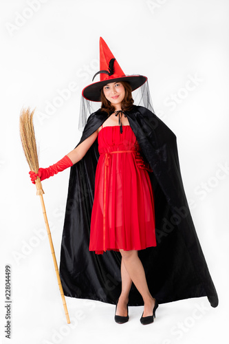 Woman witch in red witch costume holding broomstick, studio shot on white background. Concept for funny dressing in halloween festival