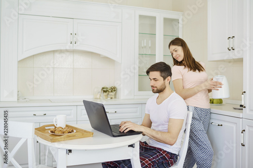 A young couple is having breakfast at the table, working with a laptop in the morning in the kitchen. photo