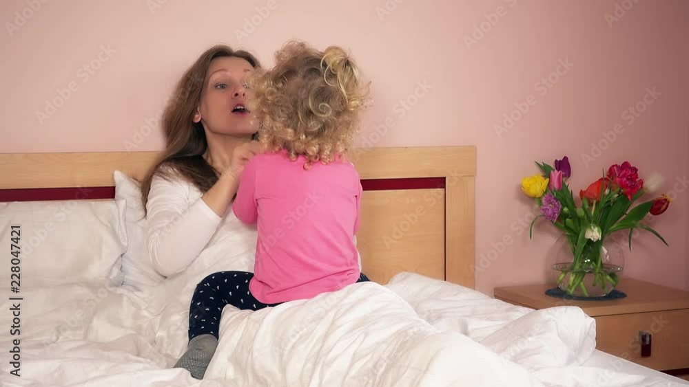 Happy mother and little daughter sitting on bed and playing Happy mother and little daughter sitting on bed and playing