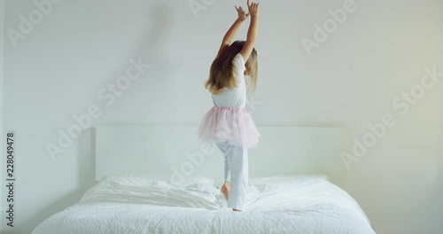 A little girl is dancing and plaA little girl is dancing and playing on her parents bed with a tutu. aying on her parents bed with a tutu. Concept: Freedom, happiness, family. Shot on Red 8K photo