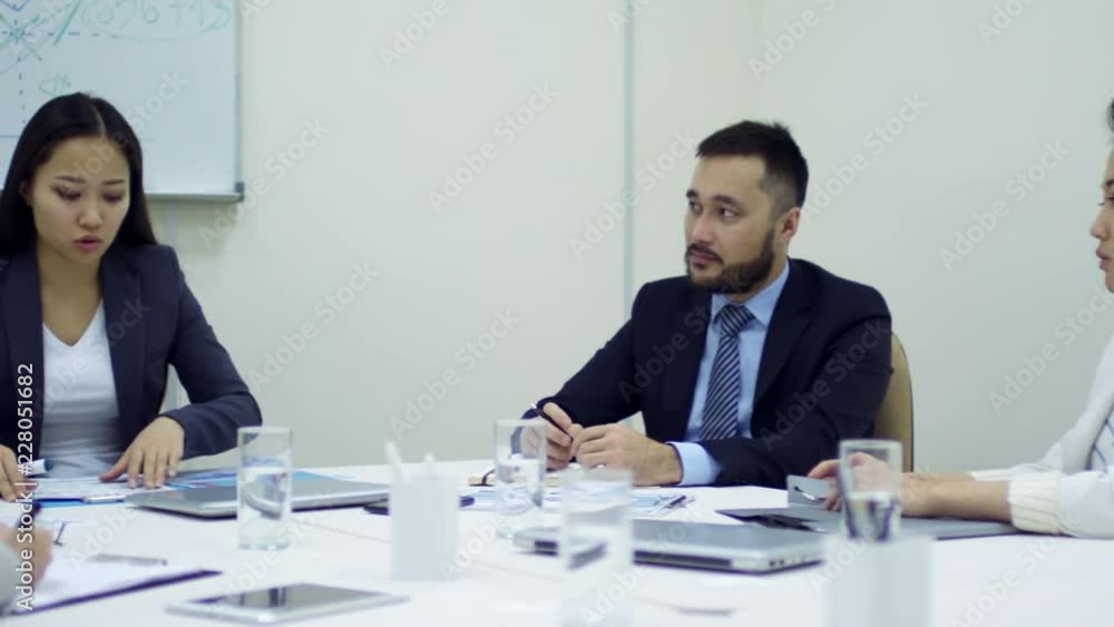 Tracking shot of group of Asian business people sitting at desk in conference room and discussing work during meeting Tracking shot of group of Asian business people sitting at desk in conference room and discussing work during meeting