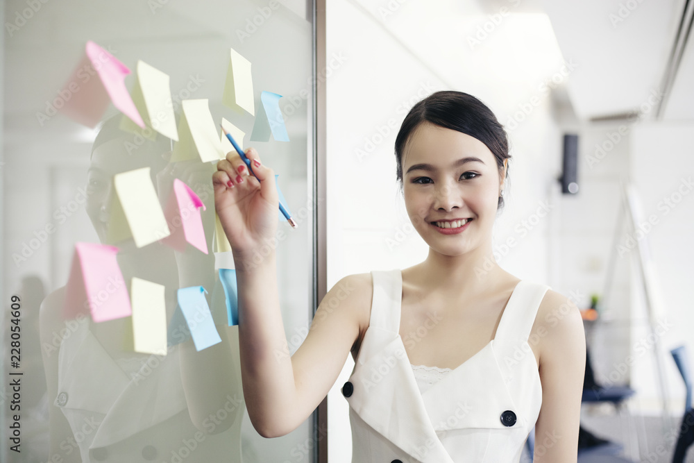 Asian business women smiling and working together on wall glass with post it stickers. Modern startup office Asian business women smiling and working together on wall glass with post it stickers. Modern startup office