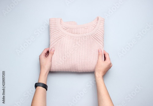Hands fold knitted sweater on a gray background. Conceptual photo. Top view.