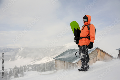 Man standing with the snowboard in hands on the hill near the house photo