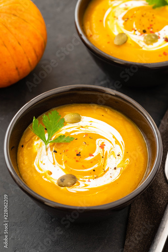 Pumpkin soup in a bowl with fresh pumpkins, garlic and parsley herbs on a black background. Autumn concept.