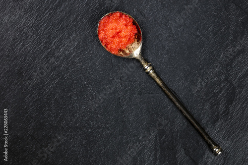 Red fish caviar in a vintage spoon, shot from above on a black background with a place for text