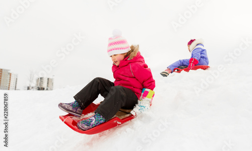 childhood, sledging and season concept - happy little girl sliding down on sled outdoors in winter