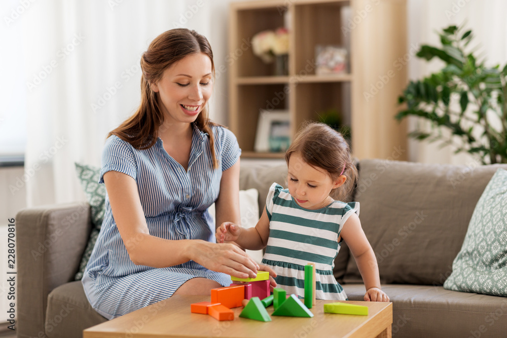 childhood and people concept - happy pregnant mother and little daughter playing with toy blocks at home childhood and people concept - happy pregnant mother and little daughter playing with toy blocks at home