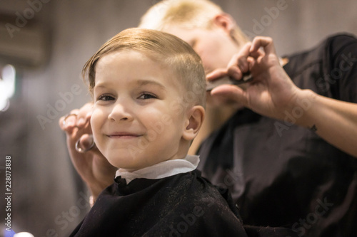 Happy little boy getting new hairstyle at barber shop.