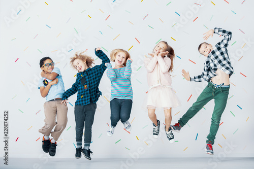 Smiling multicultural group of children jumping against colorful wallpaper