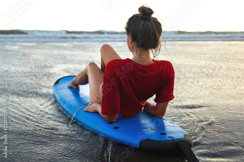 Woman sitting on surfboard on the beach after her surfing session © blackday