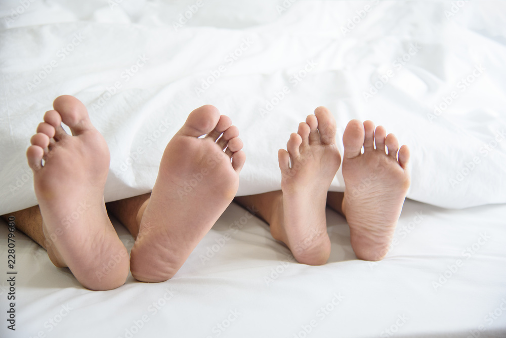 Close up of couple barefoot under blanket in bedroom in honeymoon vacation holiday in long weekend at home. Relaxation of sexual and romantic people after wedding ceremony. Valentines day love theme. Close up of couple barefoot under blanket in bedroom in honeymoon vacation holiday in long weekend at home. Relaxation of sexual and romantic people after wedding ceremony. Valentines day love theme.