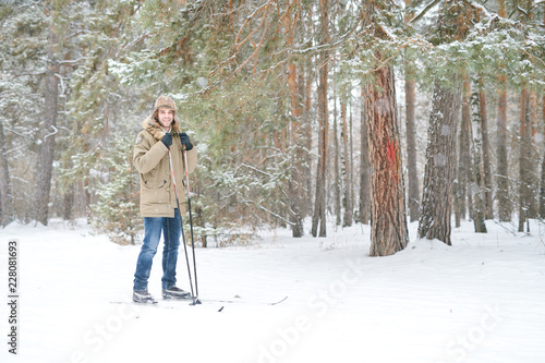 Full length portrait of happy young man smiling at camera while enjoying skiing in snowy winter forest, copy space