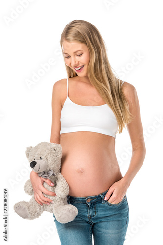 cheerful pregnant woman holding teddy bear isolated on white