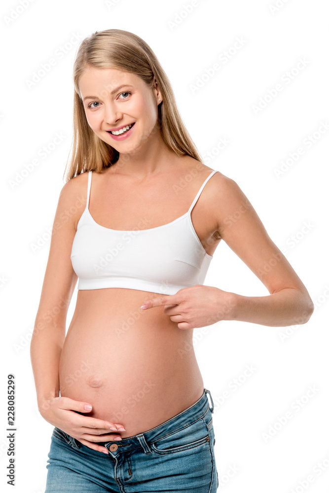 smiling pregnant woman in white bra pointing at her tummy isolated on white smiling pregnant woman in white bra pointing at her tummy isolated on white