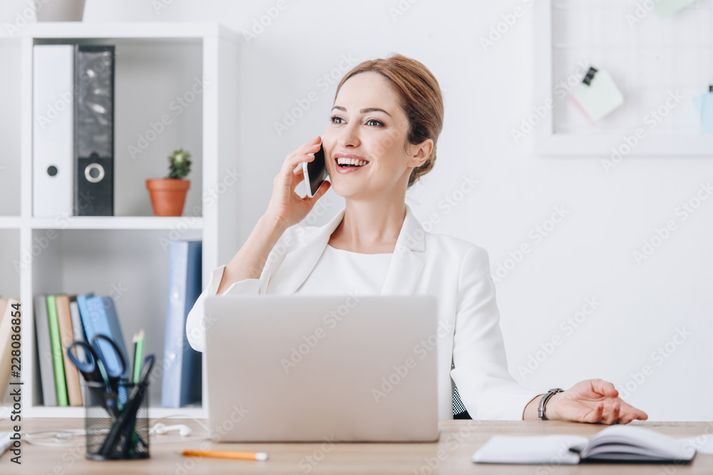 happy successful businesswoman talking on smartphone in modern office with laptop