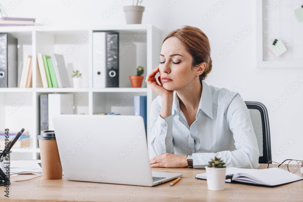 exhausted adult businesswoman sleeping at workplace in modern office while leaning on hand
