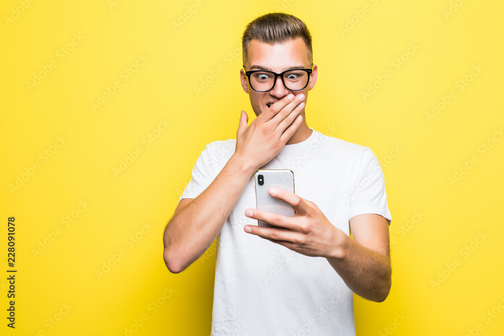 Portrait of a cheerful young man shocked on mobile phone isolated over yellow background Portrait of a cheerful young man shocked on mobile phone isolated over yellow background
