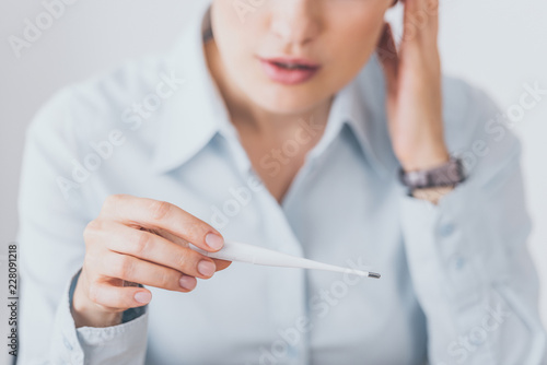 cropped shot of sick businesswoman sitting at workplace and holding electric thermometer