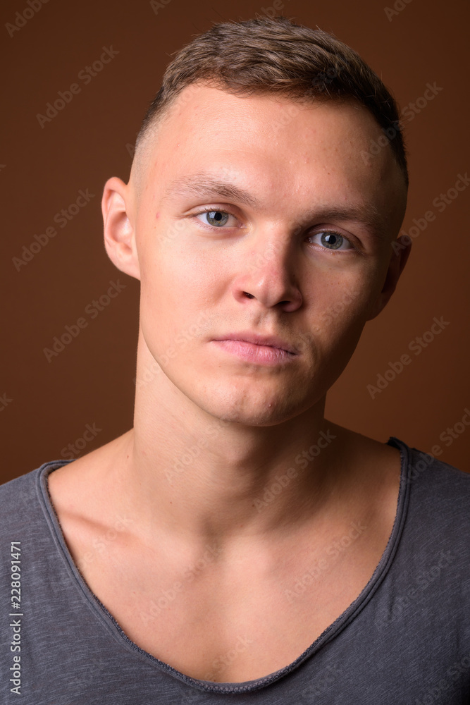 Fototapeta premium Young man wearing gray shirt against brown background