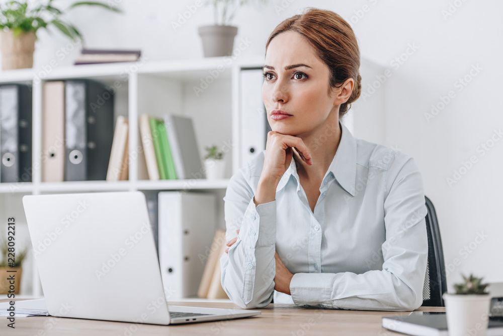 thoughtful adult businesswoman sitting at workplace at office and looking away thoughtful adult businesswoman sitting at workplace at office and looking away