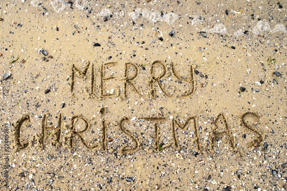 Fototapeta premium Merry Christmas written on tropical beach sand, copy space. Holiday concept, top view