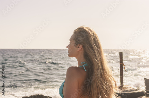 Portrait of a young woman with long hair enjoying the sunshine at sunset by the sea