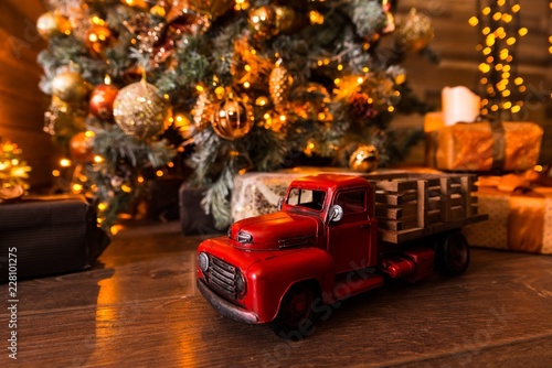 Toy car with a red body is on a wooden floor under the Christmas tree with gifts