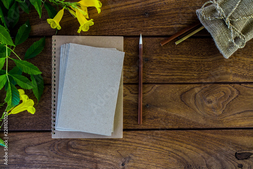 Flat lay photo of wooden desk with notebook, envelopes and flowers top view.