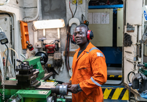 African marine engineer officer in engine control room ECR. He works in workshop with equipment