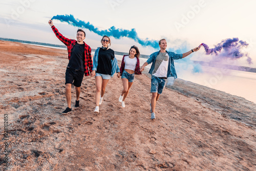 group of young friends running along the beach and holding hand flare or fusee. Freedom and independence concept