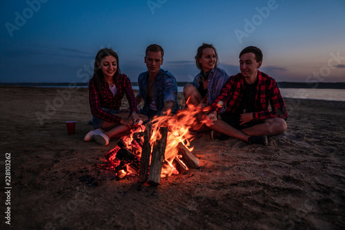 Camp on the beach. Group of young friends having picnic with bonfire. They eat marshmallows