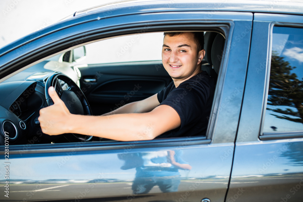 Young handsome man smiling and showing thumbs up in his car Young handsome man smiling and showing thumbs up in his car