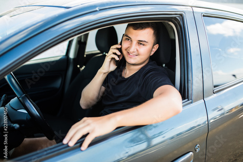 Portrait of young handsome man driving car and speaking on mobile phone.