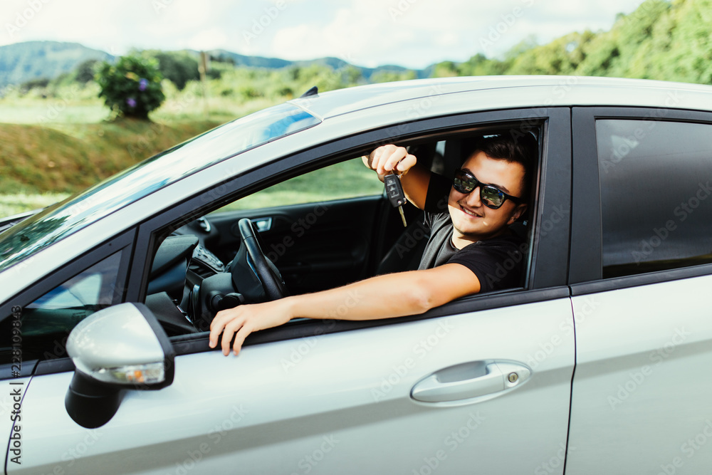 Young man in sunglasses sitting in car holding car keys outdoors